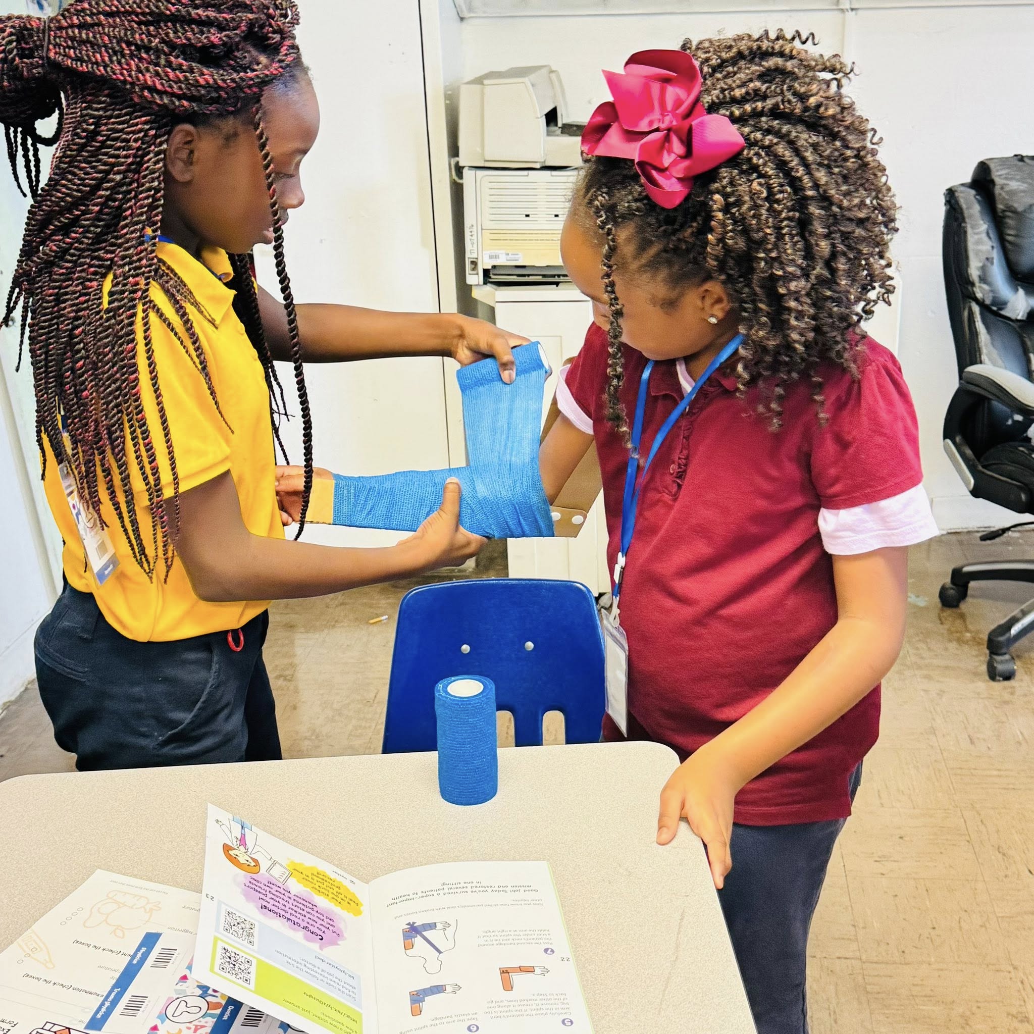 A girl putting a splint on another girl's arm.
